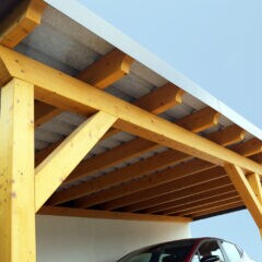 Ein Auto steht unter einem Carport aus Holz.