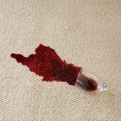 Verschütteter Rotwein auf weißem Teppich